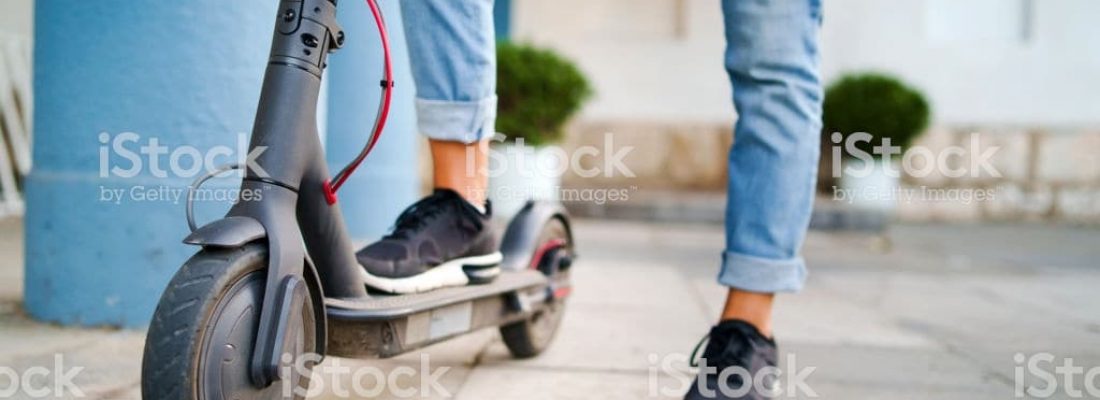 Close up on woman legs feet standing on the electric kick scooter on the pavement wearing jeans and sneakers in summer day